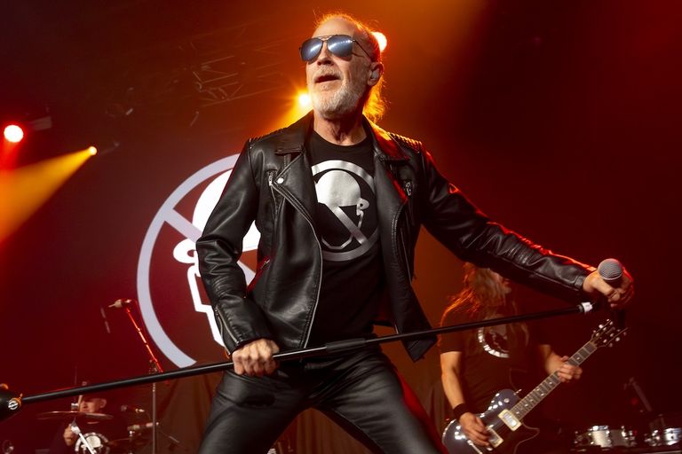 Men Without Hats lead singer Ivan Doroschuk performing live in aviator sunglasses and a black leather jacket on stage.